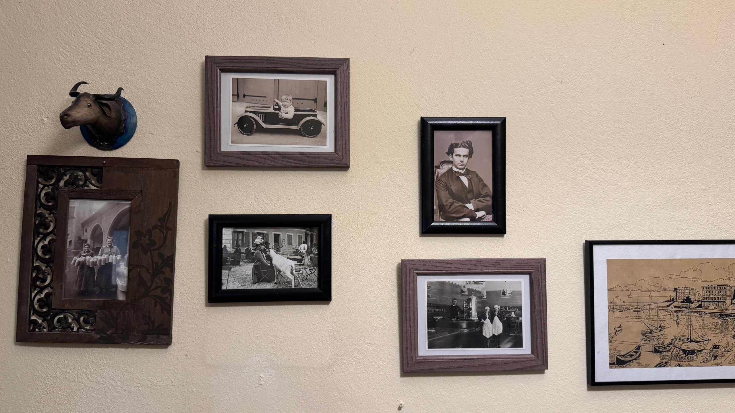 Beige wall displaying vintage black-and-white photos in wooden frames, with a mounted bull head on the left.