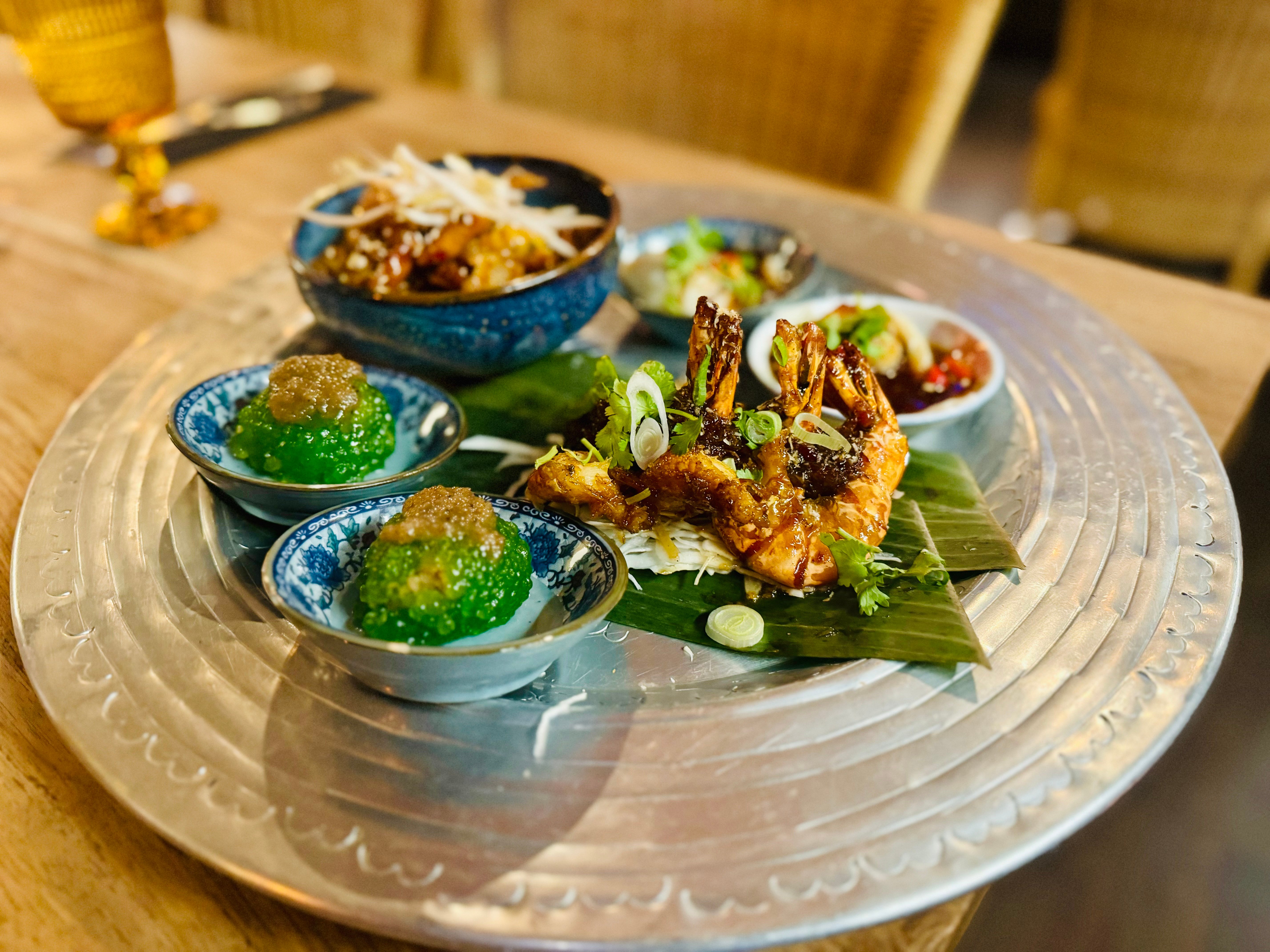 Malaysische Vorspeisen auf Silbertablett mit grünen Peanut Sagu Balls, Butter-Prawns auf Bananenblatt und Dips in Schälchen