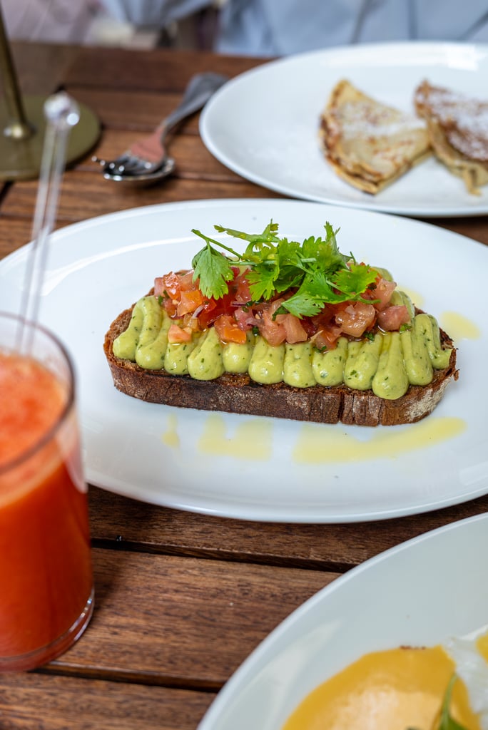 Slice of bread topped with avocado spread and diced tomato/cilantro garnish on a white plate.