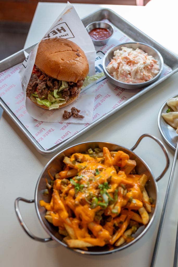 Burger with beef and lettuce in a bun on a metal tray, served with coleslaw and a bowl of cheesy fries on the side.
