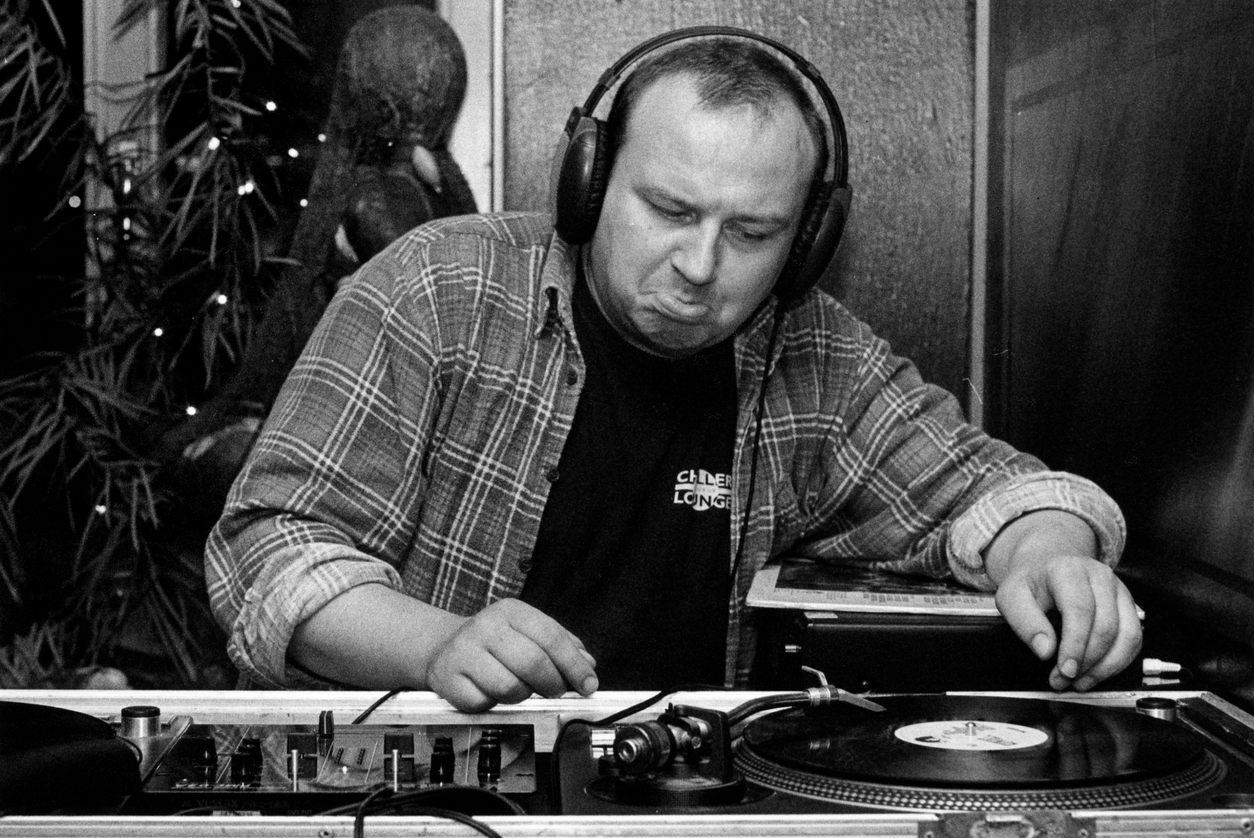 DJ wearing large headphones, mixing on turntables with vinyl records in a black-and-white scene.