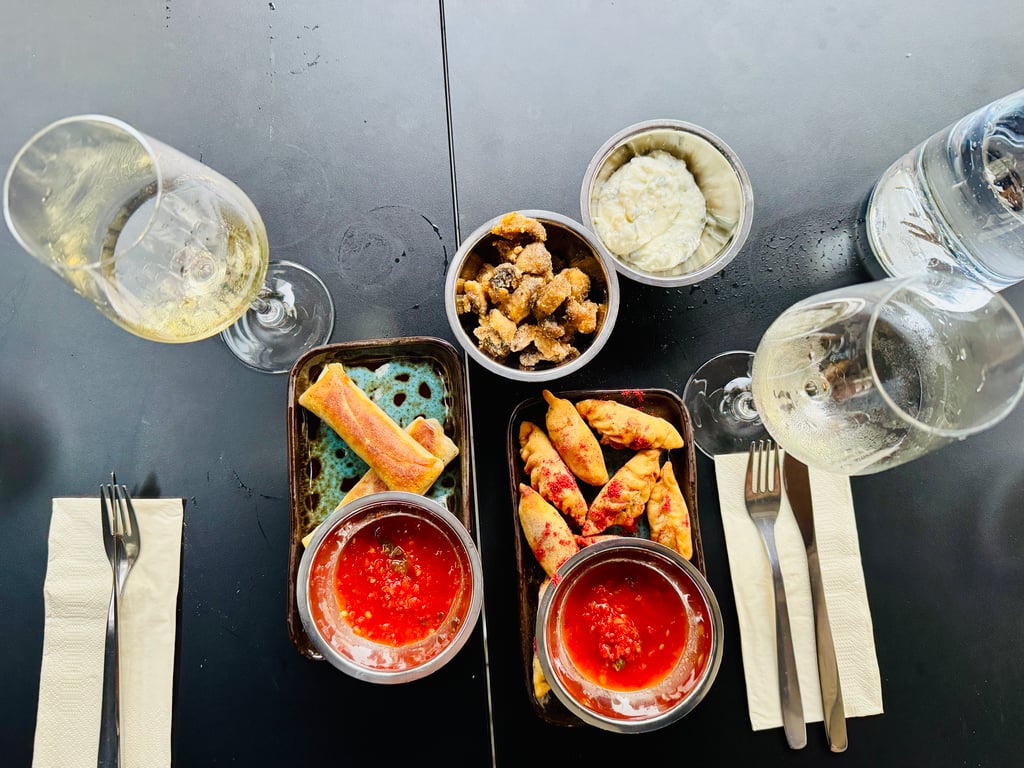 Overhead view of a dining table with three bowls of tomato soup, crispy croutons, and a creamy dip, surrounded by wine glasses and cutlery.
