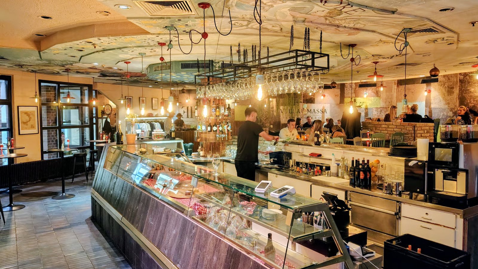 Restaurant bar interior with a long glass display case and hanging wine glasses above the counter.