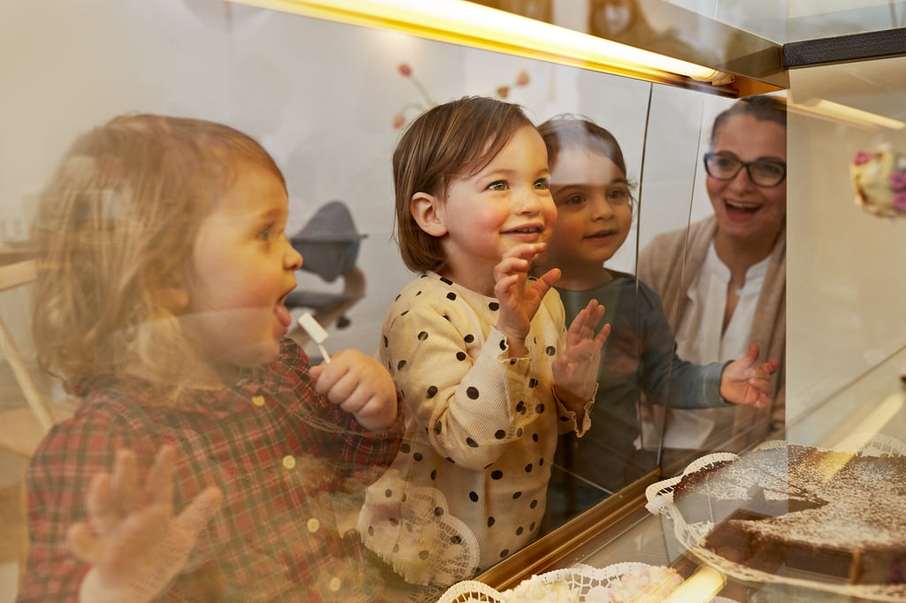 Kleinkinder stehen strahlend vor der Glasscheibe einer Kuchentheke