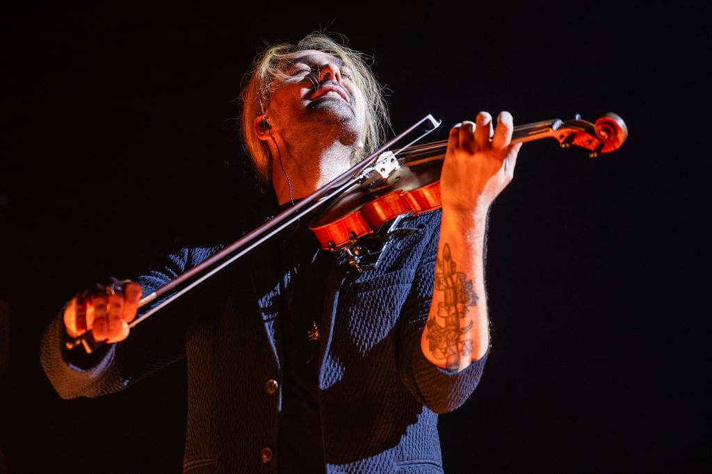 Violinist on a dark stage, head tilted back and bow in motion as he plays a wooden violin.