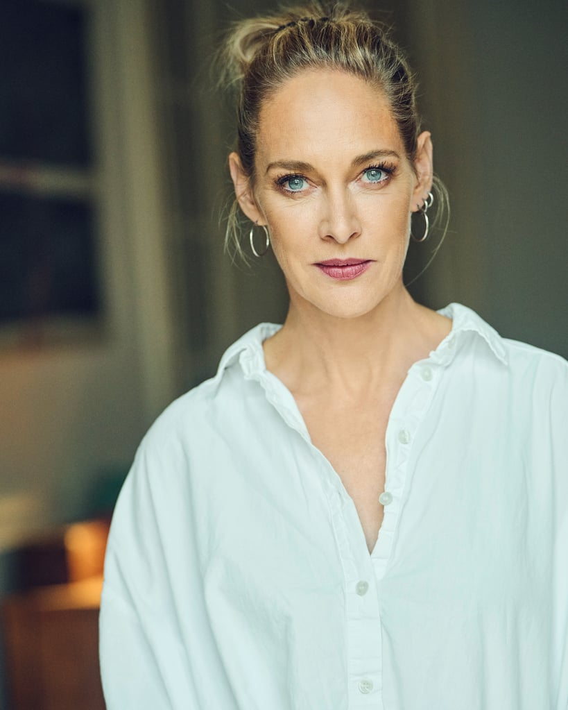 Close-up portrait of a woman with blue eyes, wearing a white button-down shirt and hoop earrings, looking at the camera.