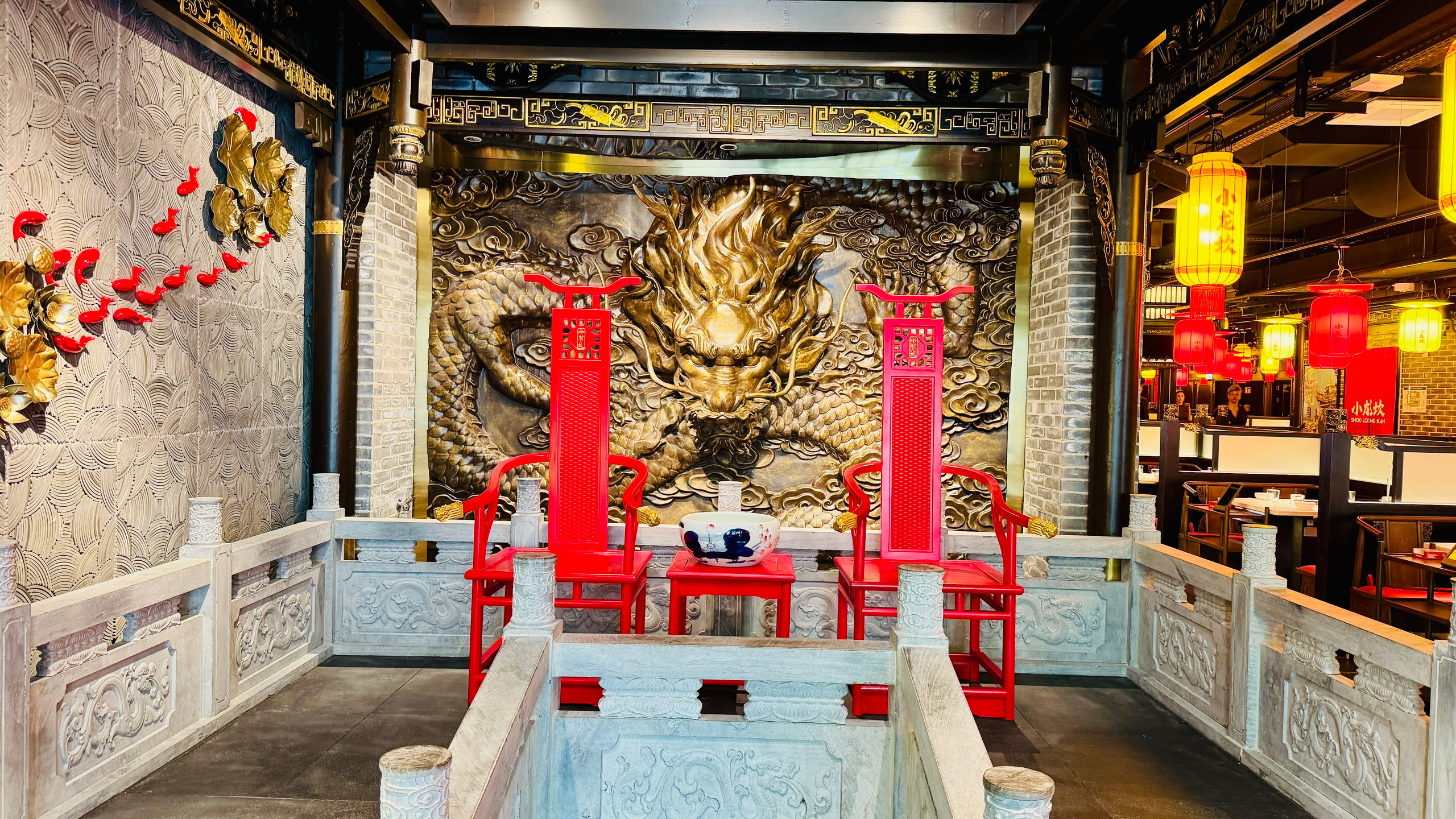 Dragon relief wall behind two tall red ceremonial chairs in a Chinese-inspired dining area with ornate gold trim.