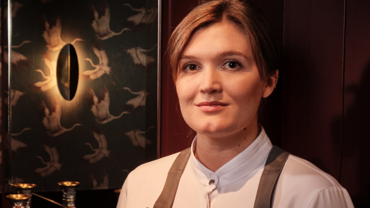 Rosina Ostler, Küchenchefin vom Alois, im Porträt vor einer Tapete mit Kranichmotiv