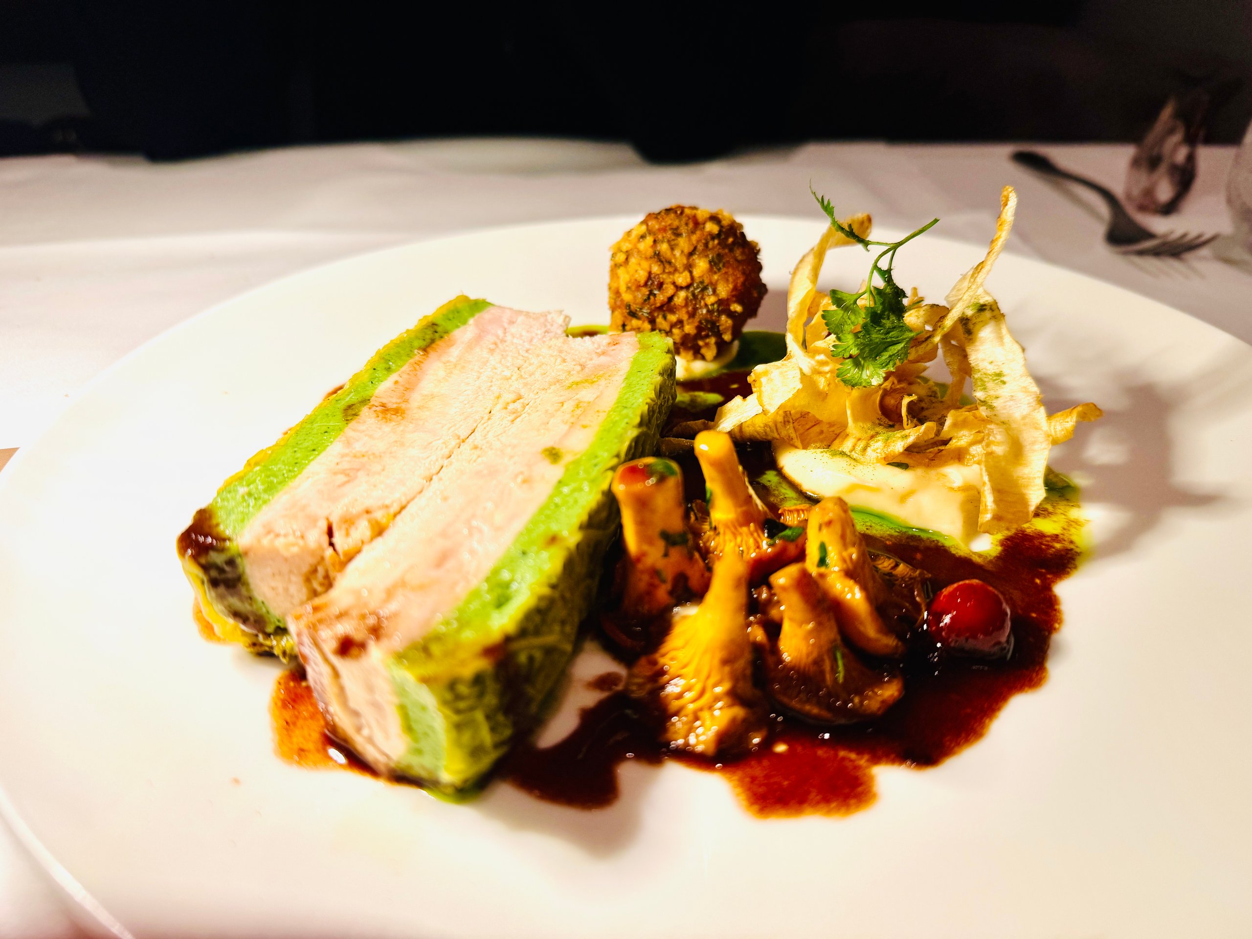 Perlhuhnroulade mit grüner Kräuterkruste, Pfifferlingen und Pilz-Arancino auf weißem Teller