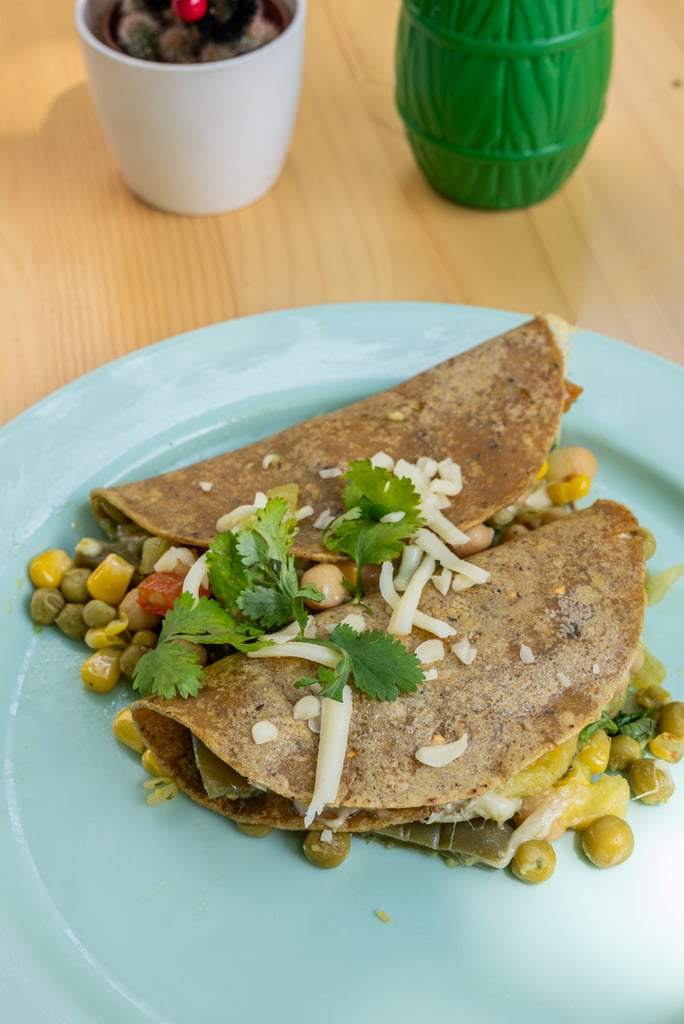 Quesadilla wedges on a light blue plate with corn, beans, cilantro and shredded cheese garnish on top of a wooden table.