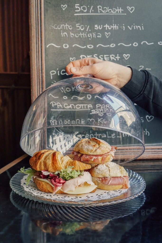Belegte Cornetti unter einer Glashaube vor der Tafel mit Tagesgerichten