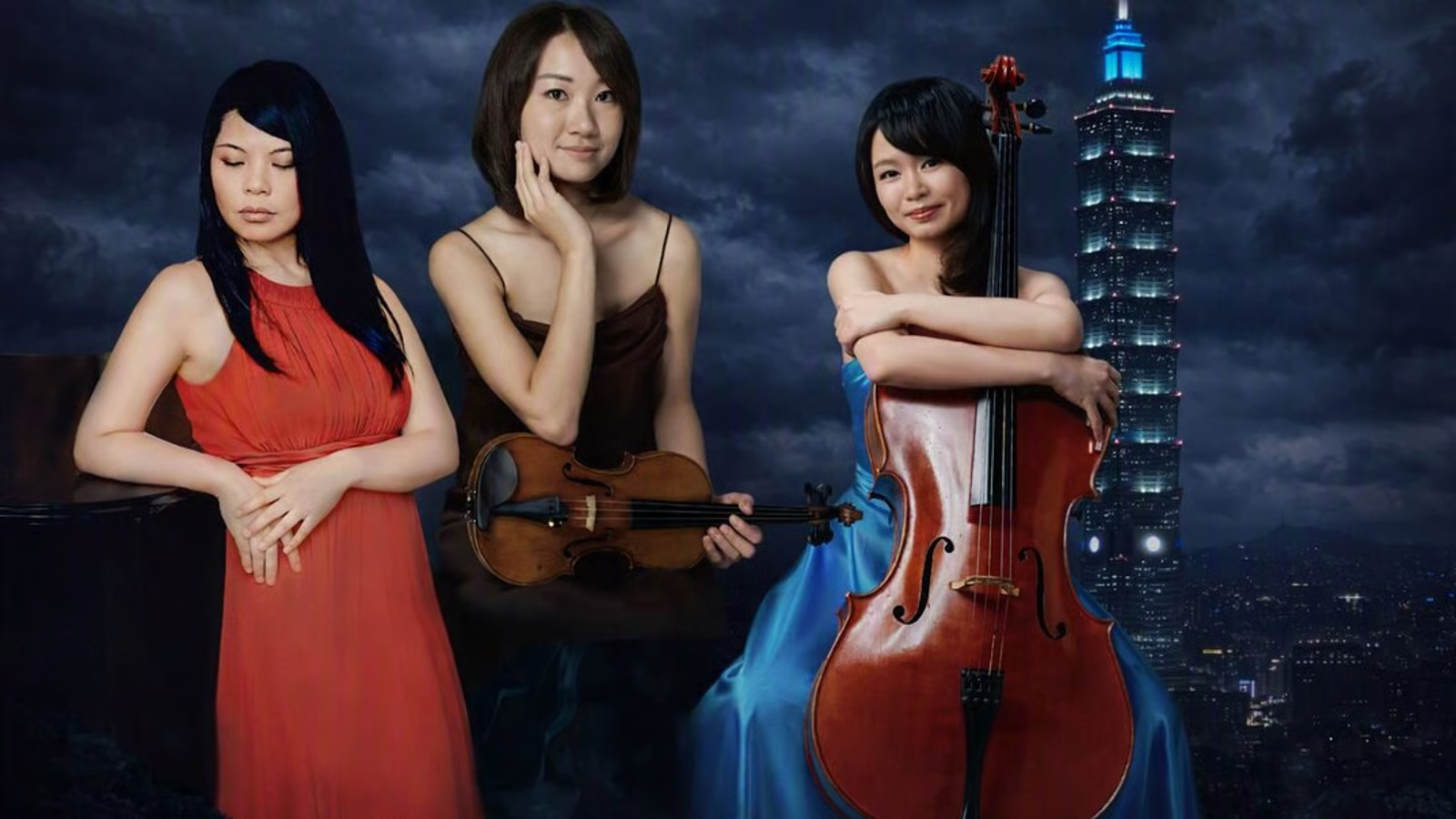 Three women musicians pose at night with a violin and a cello against a city skyline backdrop.