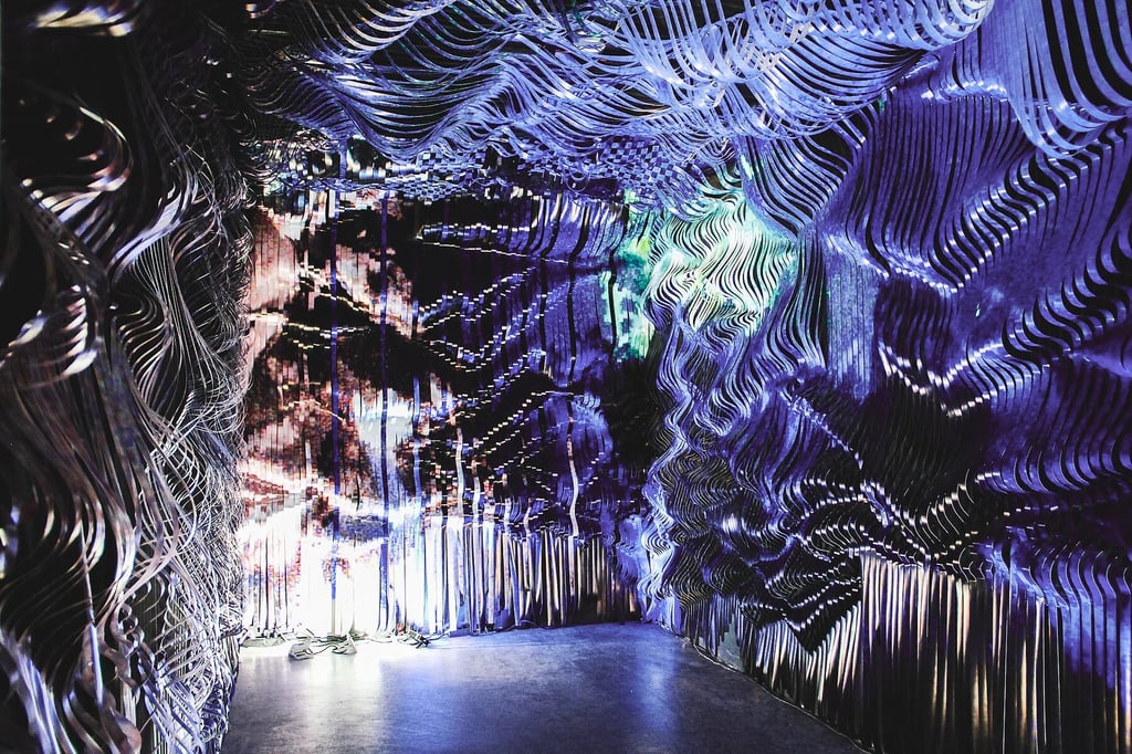 A tunnel of twisting metallic ribbons in blue and purple, forming a reflective abstract art installation.