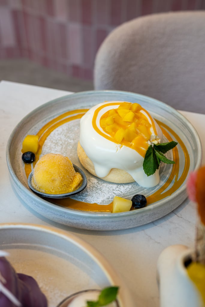 Dessert plate featuring a glossy white dome with mango cubes on top, mango sauce swirl, mint garnish, blueberries, and a dusting of powdered sugar on a blue-rimmed plate.”]}} Wait ensure not too long and correct quotes. Provide multiple options. Let's craft properly. I'll produce three options. Use straight quotes. Let's redo. 1)