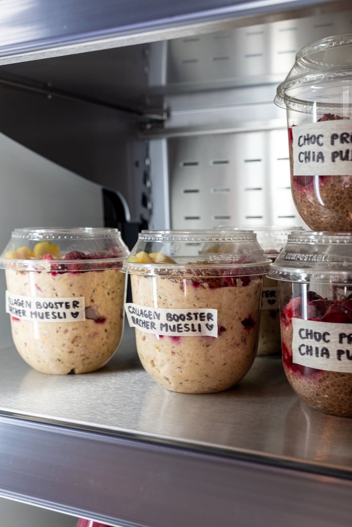 Glass jars filled with layered overnight oats in a refrigerator, labeled 'Collagen Booster Chia Muesli' with berry toppings nearby.