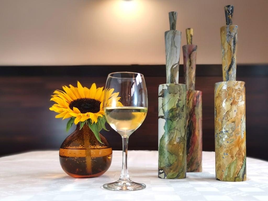 Sunflower in a brown vase beside a wine glass of white wine on a table, with marble-patterned cylinders in the background.