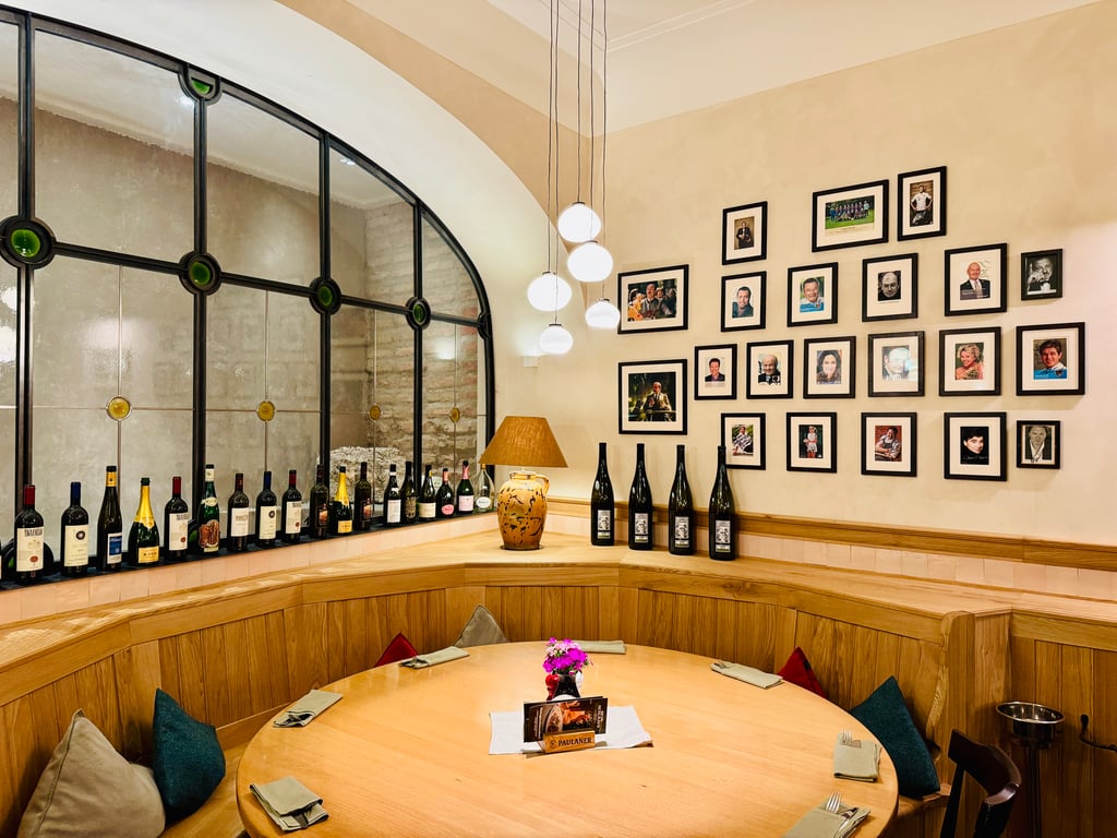 Wine bar interior with a curved glass wall, hanging globe lamps, and bottles lined along a wooden counter; photo gallery on the wall behind.