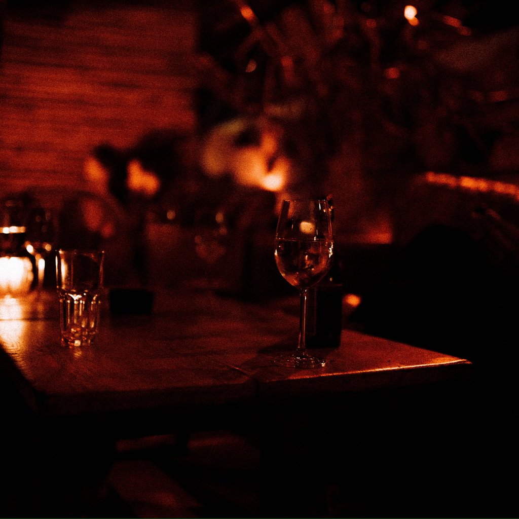 A gl glass of white wine on a wooden table in a dim bar setting with warm orange lighting