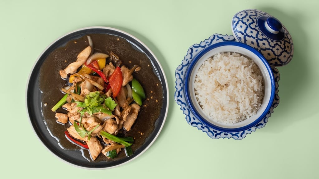 Stir-fried chicken with peppers and greens in dark soy sauce served beside a blue-and-white ceramic bowl of white rice on a pale green background