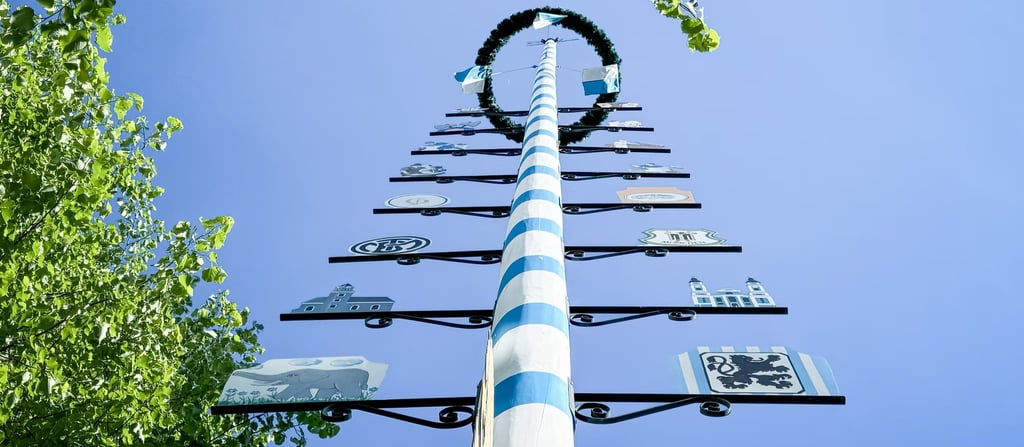 Low-angle view of a tall blue-and-white striped maypole with emblems along its length against a clear blue sky.