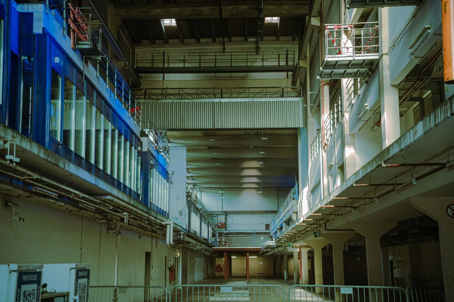Interior of a large industrial space with metal catwalks, railings, and exposed pipes along the walls.