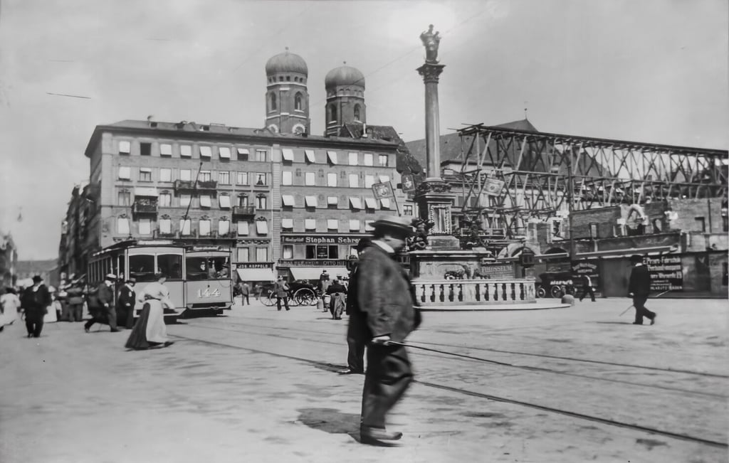 Black-and-white city square with a tram, a tall column monument, and a building with onion-domed towers; pedestrians fill the scene.