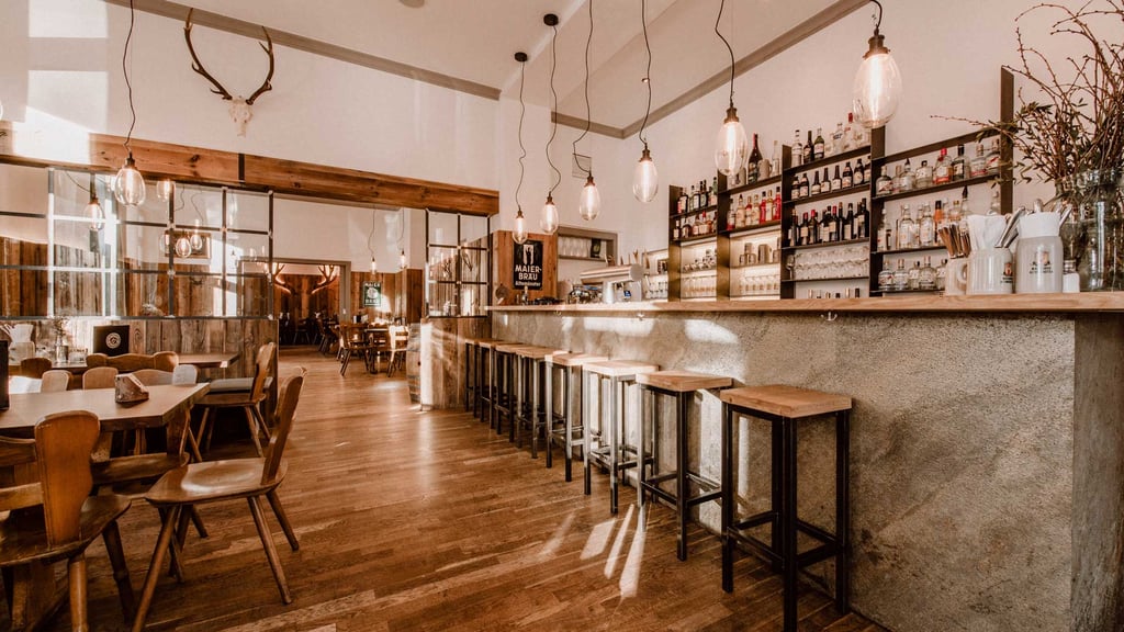 Warm wooden bar interior with liquor shelves, hanging bulbs, and a row of high stools along the counter