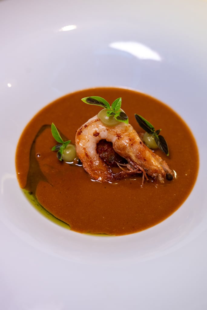 Shrimp topped with greens on a brown sauce in a white bowl, gourmet plating.