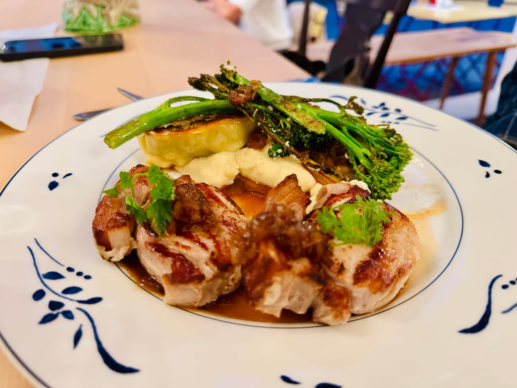 Plate with roasted pork, creamy mashed potatoes, and grilled asparagus, garnished with herbs on a patterned white plate