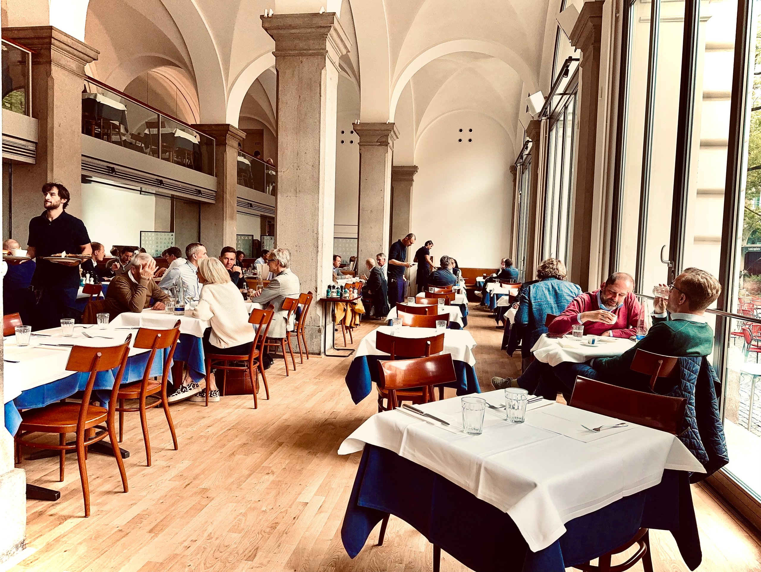 Heller Gastraum der Oskar Maria Brasserie mit Kreuzgratgewölbe, Säulen, eingedeckten Tischen und großen Fenstern