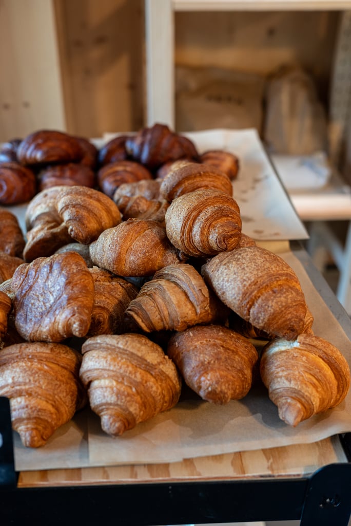 Pile of golden croissants on parchment in a bakery display case, ready for sale.