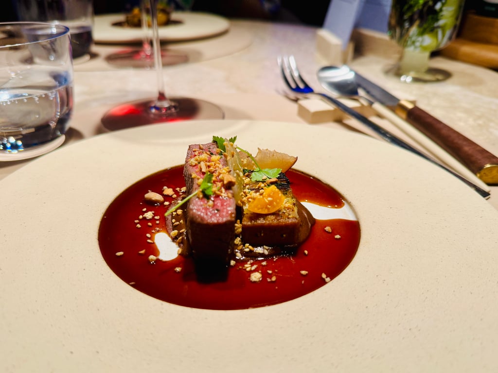 Beef steak plated on a white dish with a glossy red sauce, sprinkled with crushed nuts and green herbs as garnish.