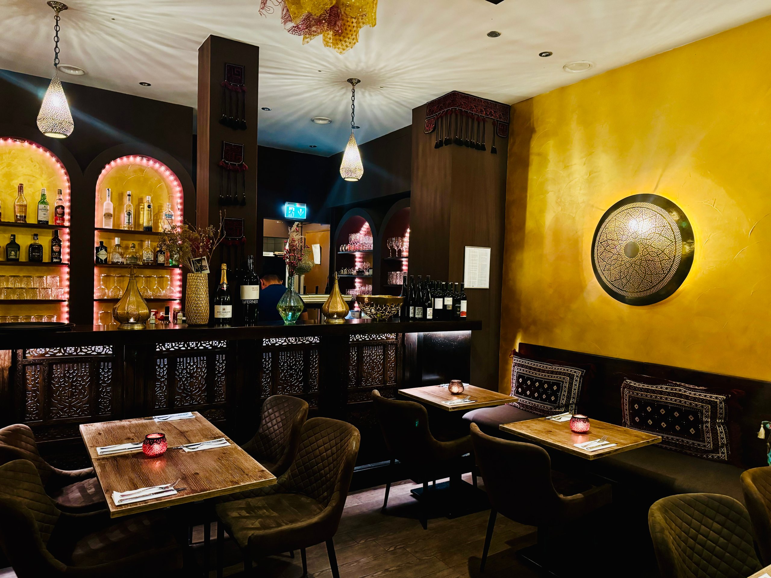 Gastraum des Hewad mit Holztischen, beleuchteten Bogenregalen an der Bar und goldener Wand