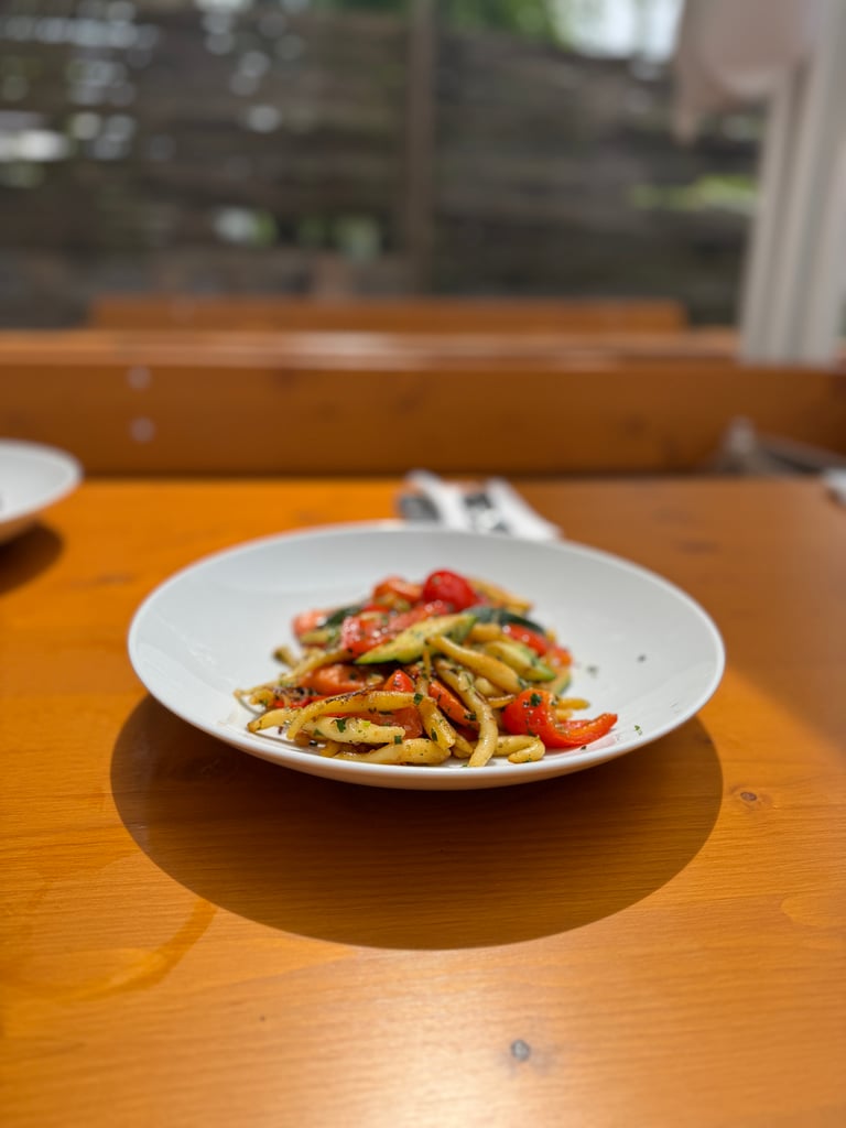 Plate of pasta with cherry tomatoes and herbs on a wooden table.