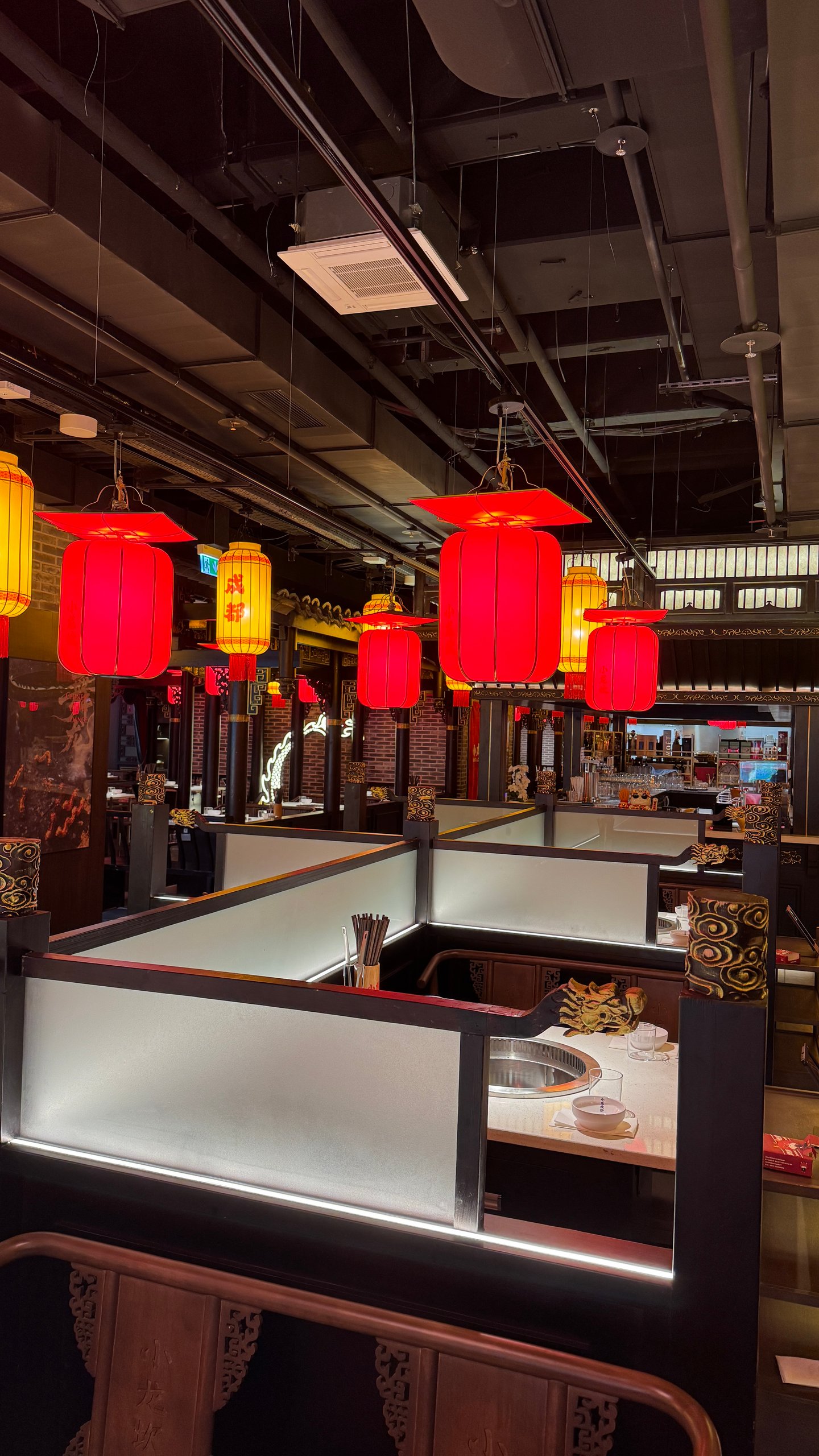 Red and yellow lanterns hang above dining booths in a modern Asian restaurant, warm and welcoming lighting.