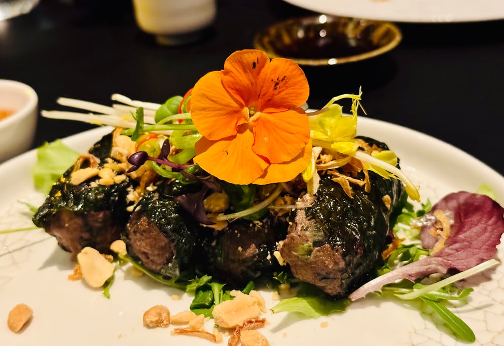 Plated dish with greens, nuts, and an orange edible flower garnish on top.
