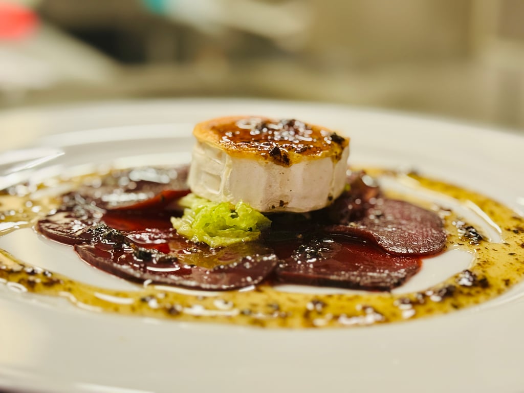 Seared foie gras on a greens bed with beet purée and plate garnish on a white dish (close-up).