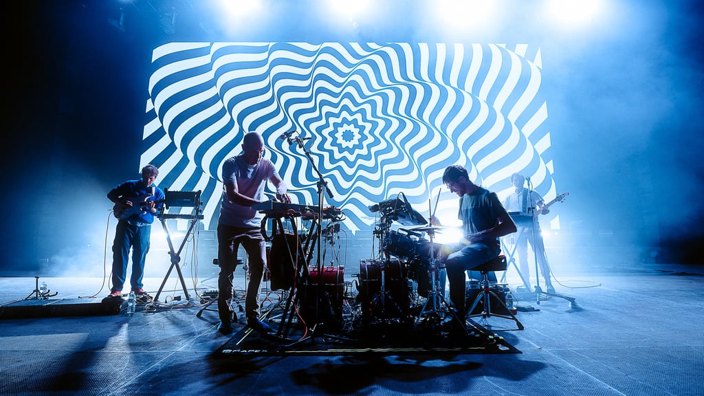 Concert on stage with four musicians and a blue, swirling optical backdrop behind them