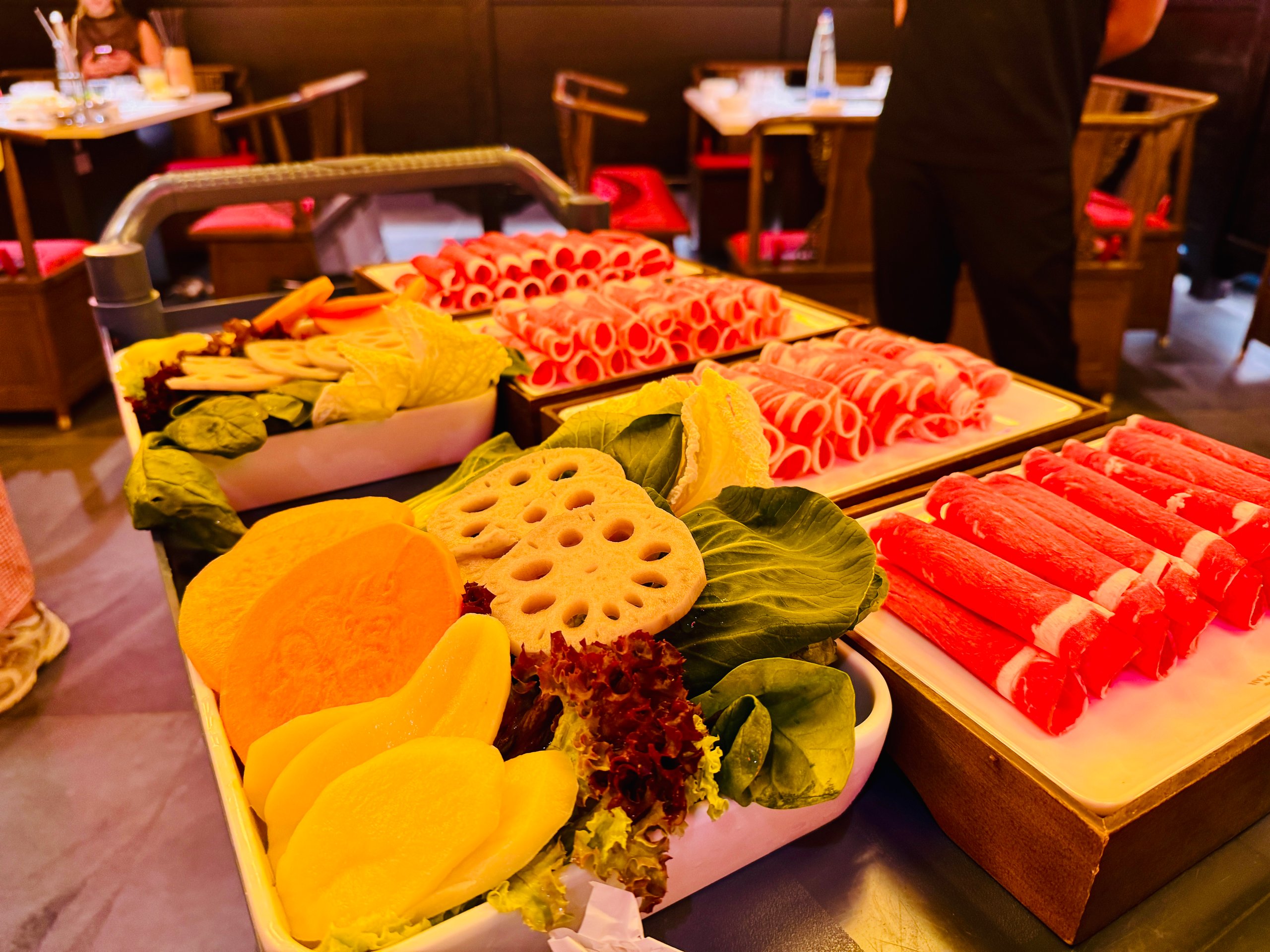 Buffet display with rolled beef slices, lotus root chips, and leafy greens on trays