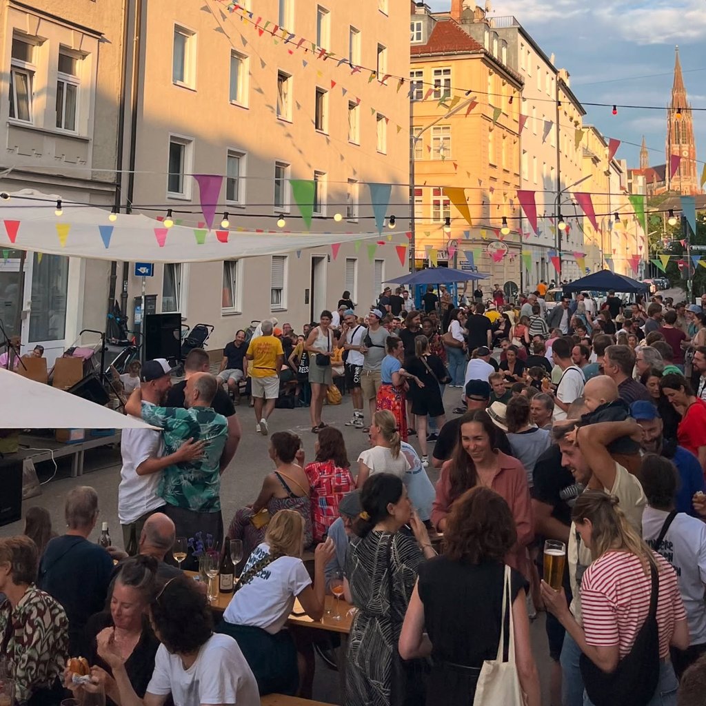 Crowded street festival with colorful bunting and string lights among pastel buildings,