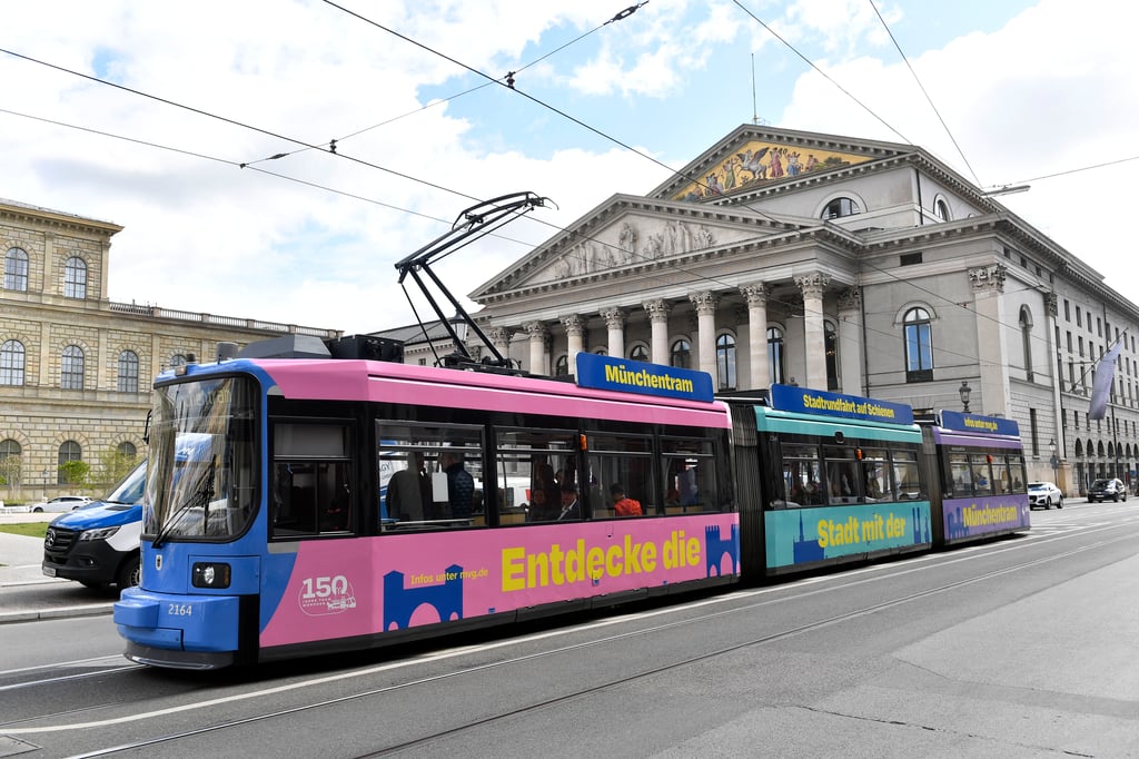 Colorful tram with pink, blue, and yellow panels on a city street in front of a neoclassical building with columns.
