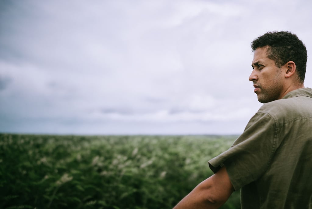 Profile of a man in a green shirt looking toward the horizon over a grassy field under a cloudy sky.
