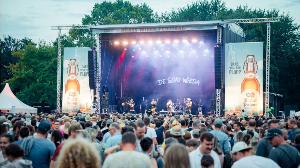 Outdoor music festival crowd watching a live band on stage with bright lights and banners on the sides.