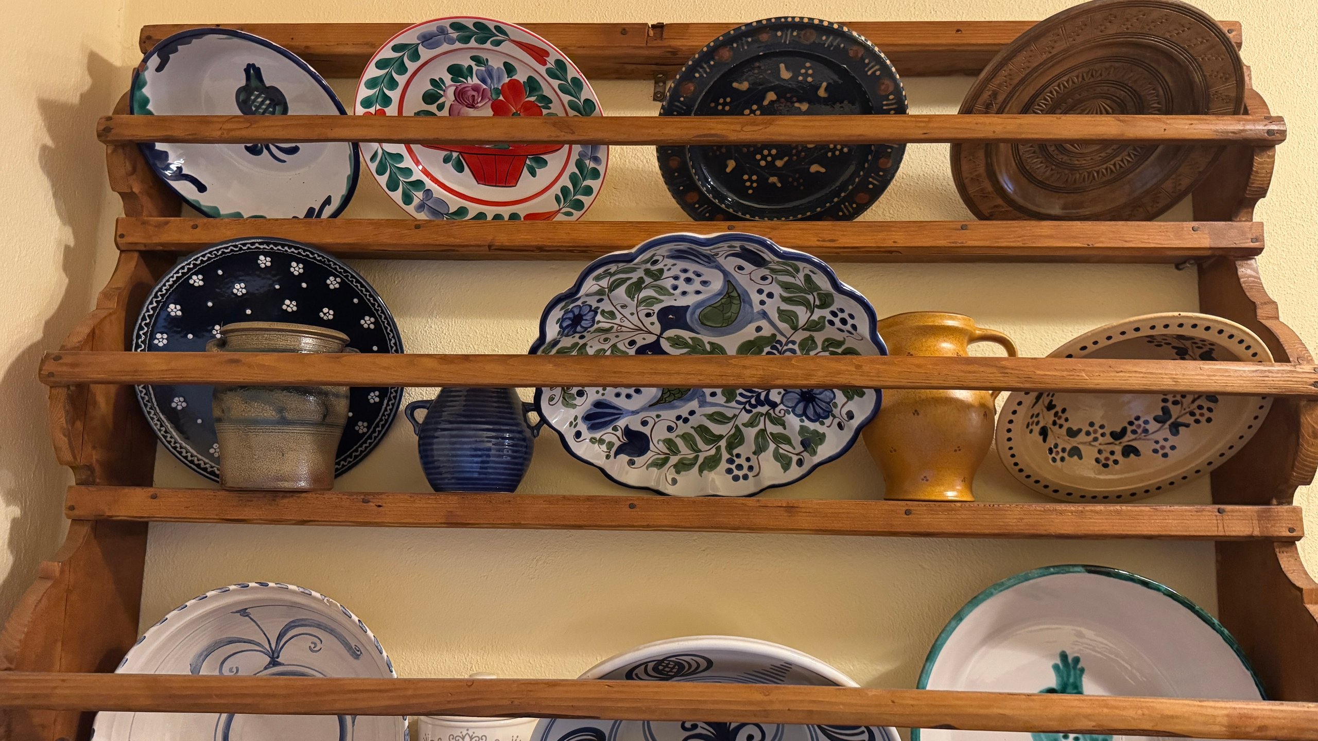 Wooden wall rack displaying decorative ceramic plates and bowls with blue, white, and floral patterns.