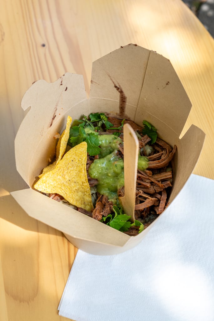 Shredded beef and cilantro in a brown takeout container with tortilla chips and a drizzle of green sauce/guacamole.