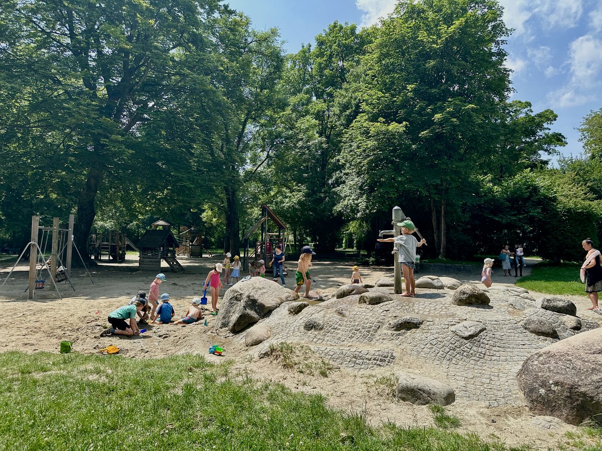Kinder spielen mit Wasserpumpe und im Sand auf dem Spielplatz im Kronepark in München an einem sonnigen Sommertag