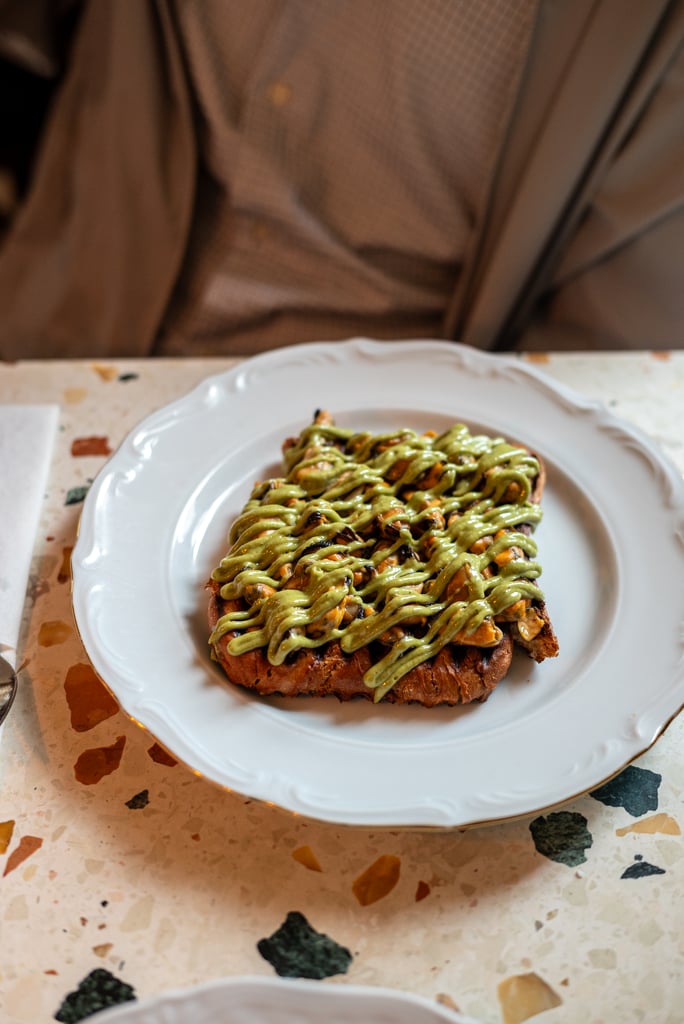 Toast slice topped with a green herb sauce and diced vegetables on a white plate.