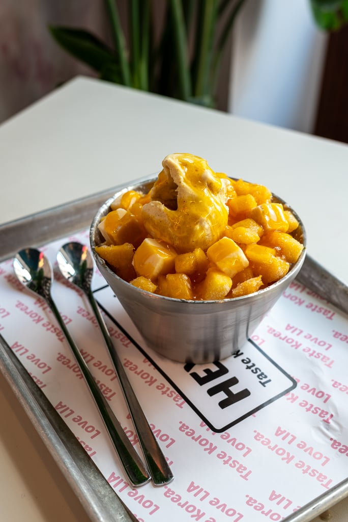 Metal cup of diced mango topped with vanilla ice cream and mango sauce on a tray.