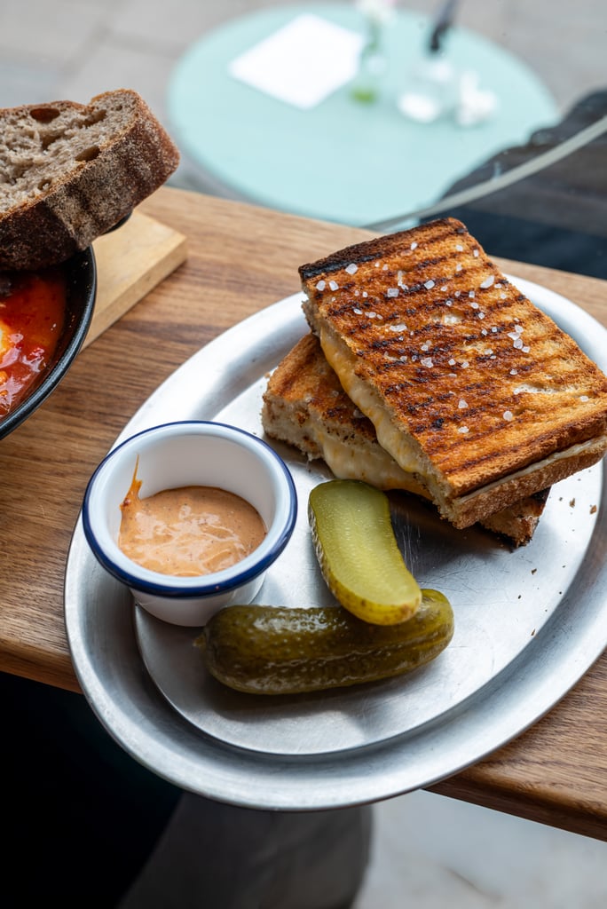 Toasted grilled cheese on a metal tray with pickles, sauces, and salt flakes on top of the bread.