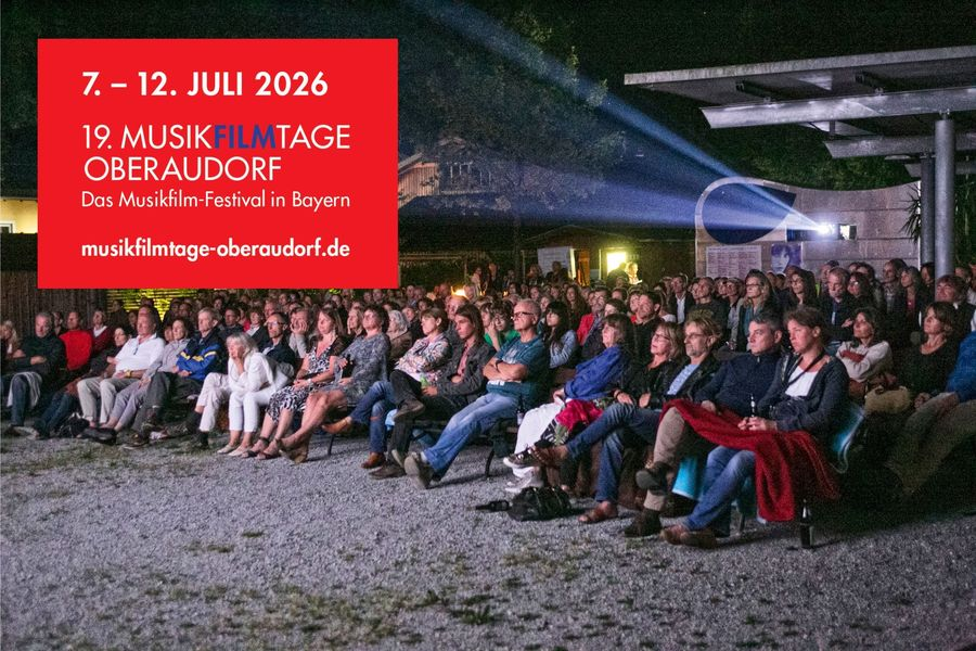 Night outdoor audience watching a screening; a large red poster in German lists dates July 7–12, 2026 and '19. MusikfilmTage Oberaudorf' with the festival URL in Bayern.